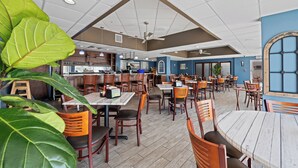 Un restaurante espacioso con mesas y sillas de madera, una zona de bar y ventiladores de techo.