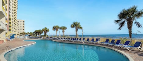 A swimming pool with lounge chairs, palm trees, and a view of the ocean.