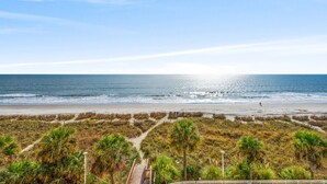 A beach view with a boardwalk leading to the shore, palm trees, and a clear sky. - Bay Watch 415-3BR/3BA Oceanfront Condo in North Myrtle Beach (North Myrtle Beach)