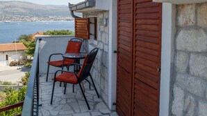 A balcony with a stone floor, a table with chairs, and a view of the sea and distant hills. - A2 - Studio With Balcony, Just 3 min to the Beach (Okrug)