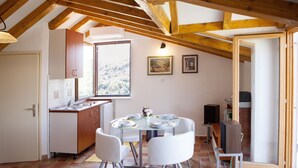 A dining area with a table set for four, white chairs, a wooden ceiling, and a window overlooking a snowy landscape. - A2 - Studio With Balcony, Just 3 min to the Beach (Okrug)