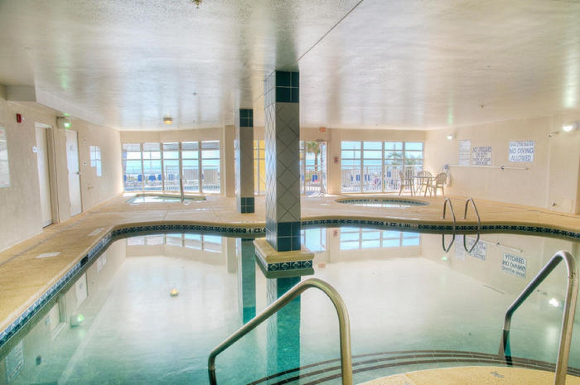 A large indoor swimming pool with clear glass walls, a tiled floor, and a pool ladder.