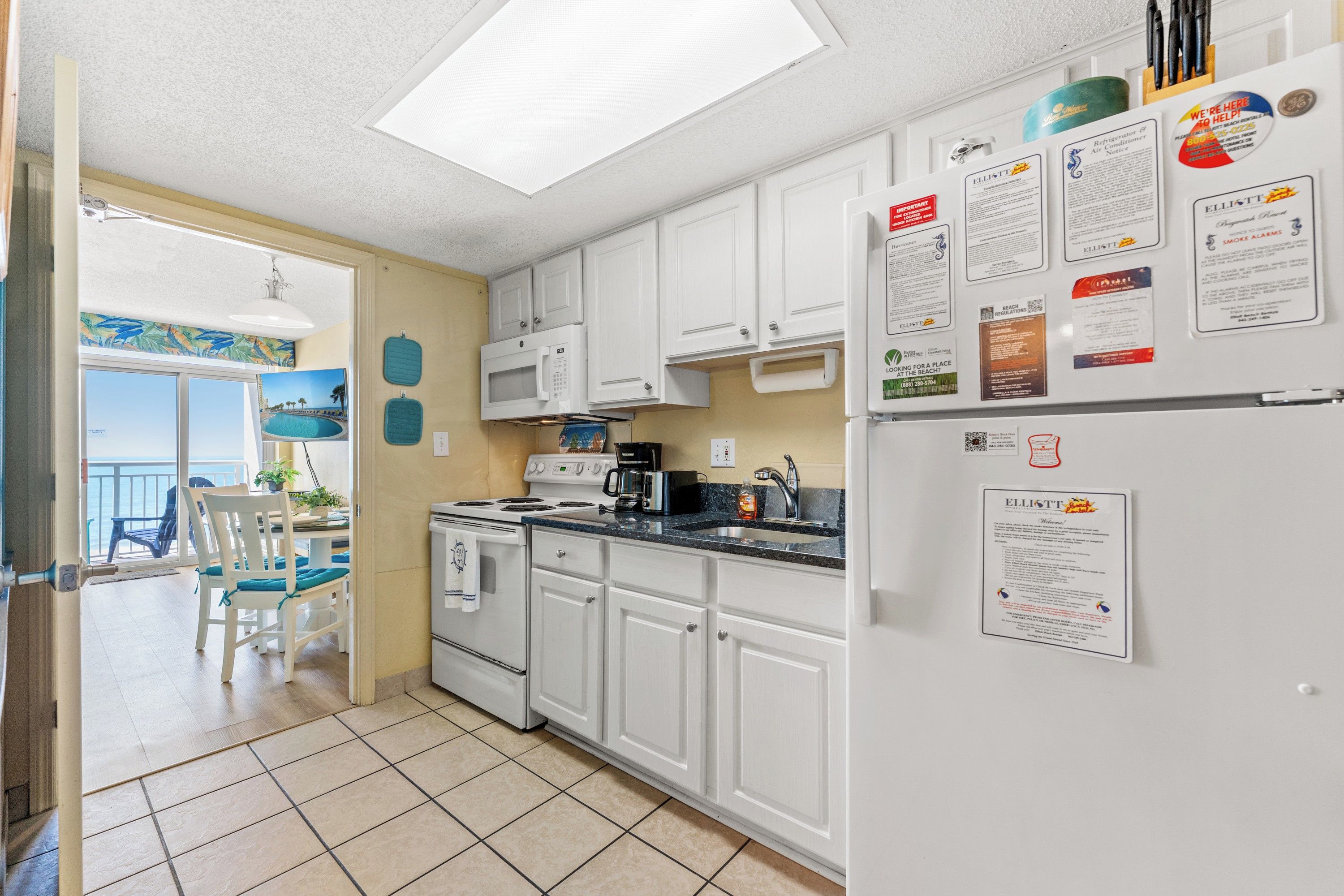 A kitchen with white cabinets, a microwave, stove, and a refrigerator. There are various notices and signs on the refrigerator door.
