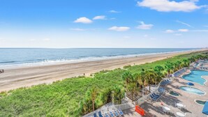 Een resort met een zwembad, ligbedden en uitzicht op het strand.