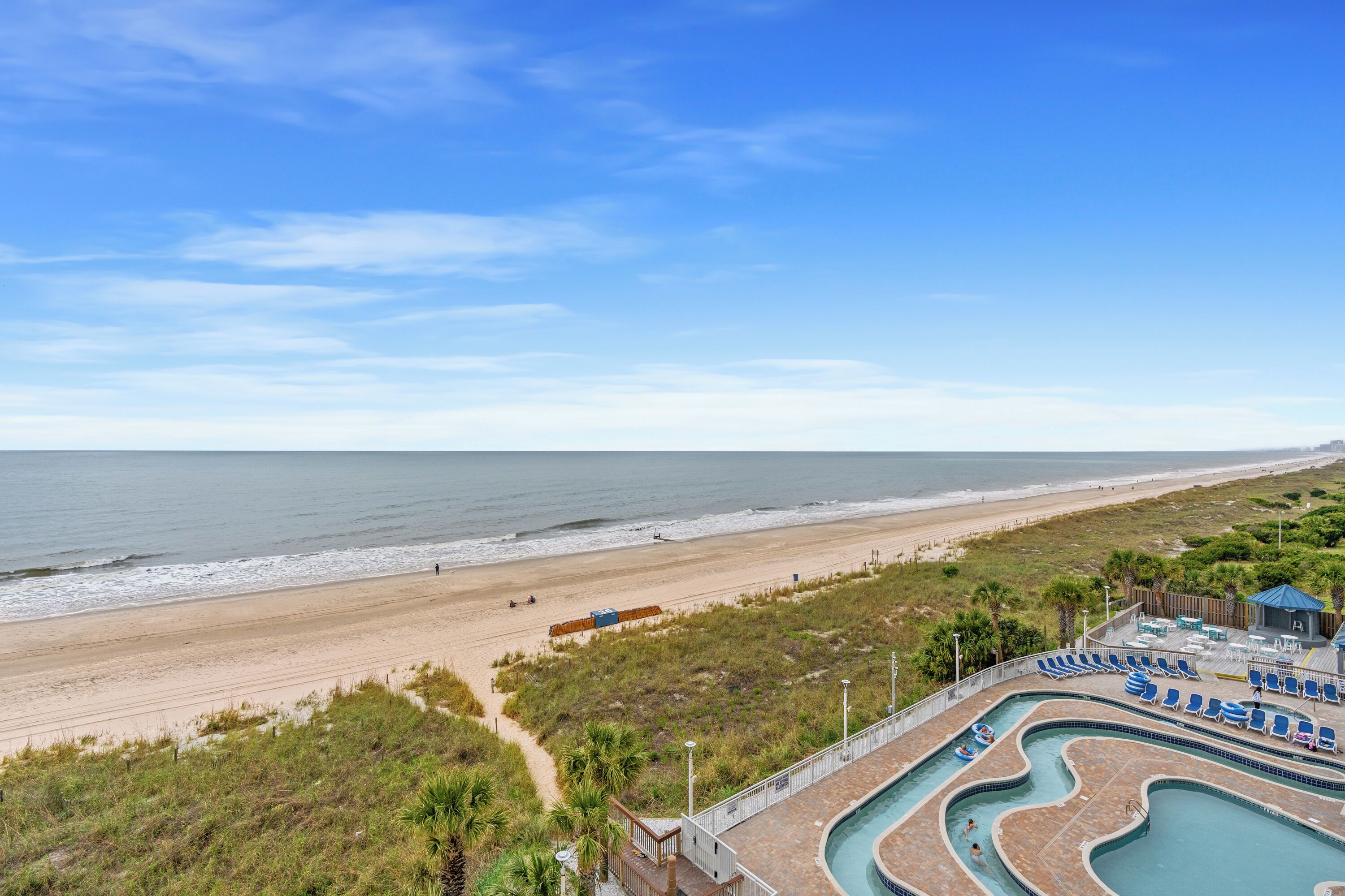 A beachside resort with a swimming pool, lounge chairs, and a view of the ocean.