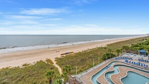 A beachside resort with a swimming pool, lounge chairs, and a view of the ocean.