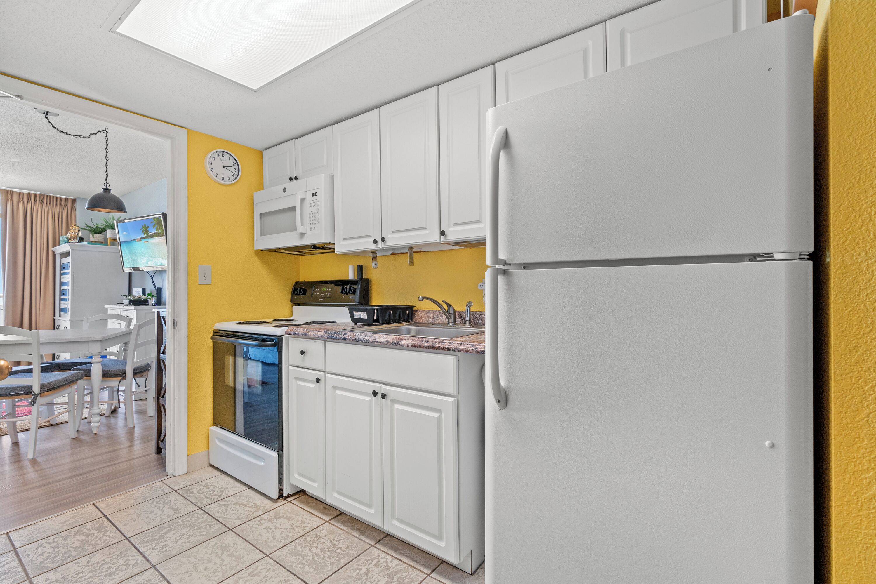 A compact kitchen with white cabinets, a built-in microwave, and a refrigerator.