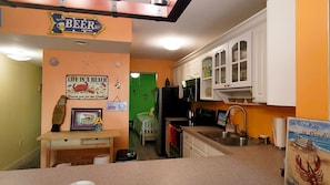 Una cucina compatta con una parete verde, un cartello con la scritta 'Life is a Beach' e un cartello che indica un'area bar con la scritta 'Beer'.