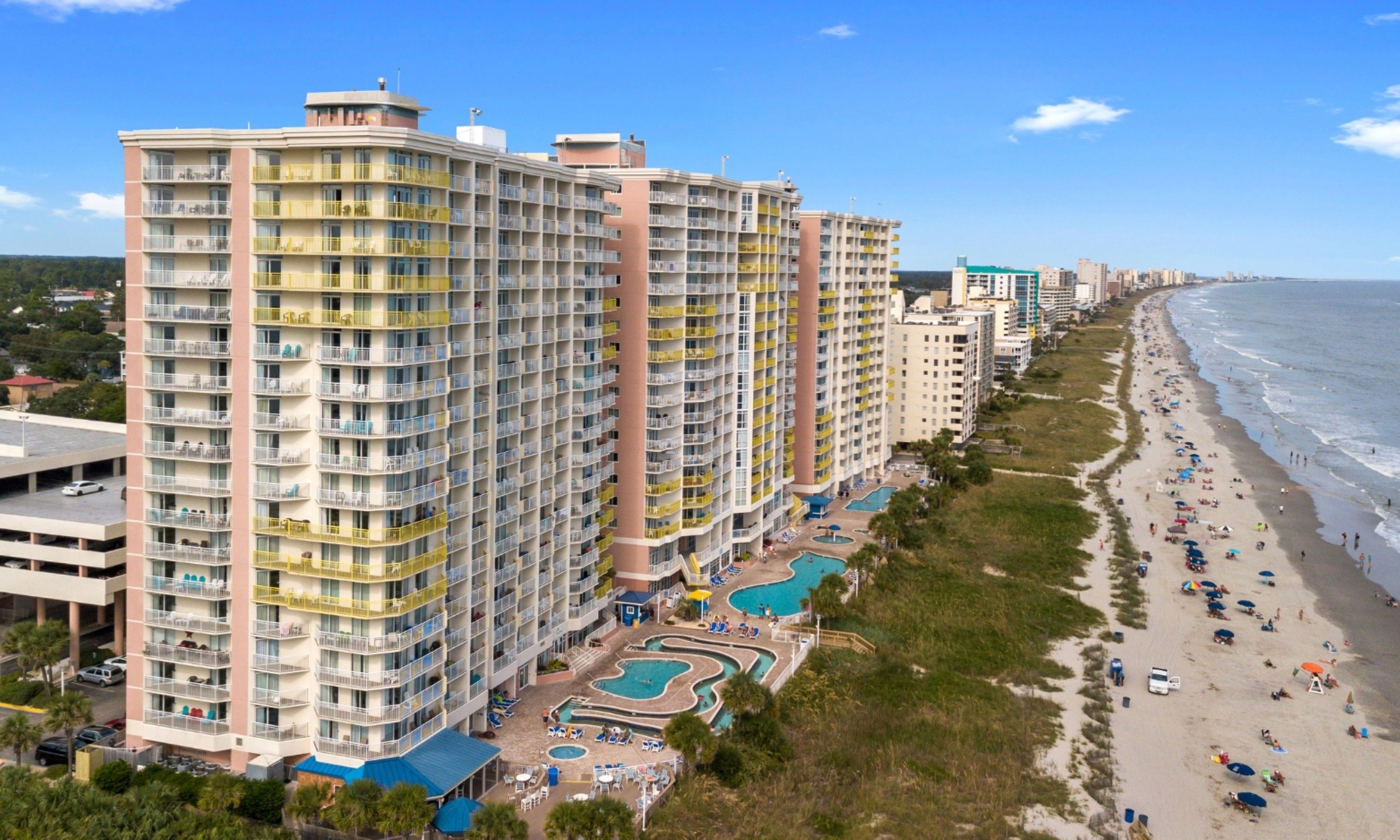 Ein Hochhaus-Hotel mit mehreren Balkonen, einem Poolbereich und einer Lage direkt am Strand.
