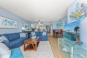 A living room with a blue sofa, a wooden coffee table, and a glass TV stand. - Bay Watch 805-3BR/2BA Oceanfront Condo in North Myrtle Beach (North Myrtle Beach)