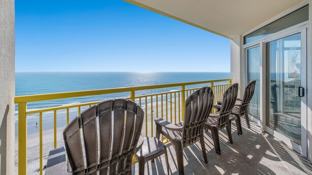A balcony with chairs and a table overlooking a beach and ocean.