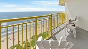 A balcony with a yellow railing overlooking a beach with people and umbrellas.