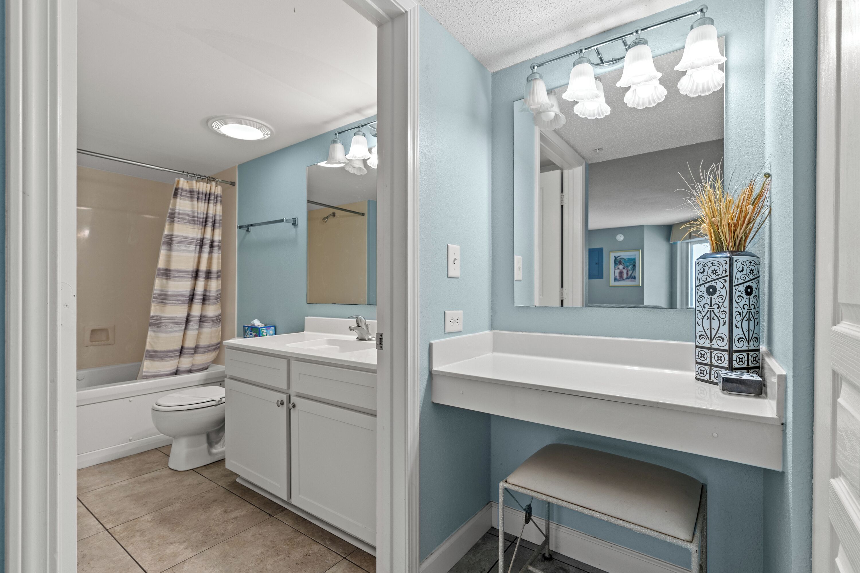 A bathroom with a bathtub, toilet, vanity, and a mirror with lights.