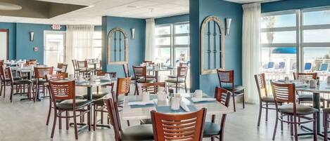 Un amplio comedor con múltiples mesas y sillas, ventanas grandes y vistas al exterior.