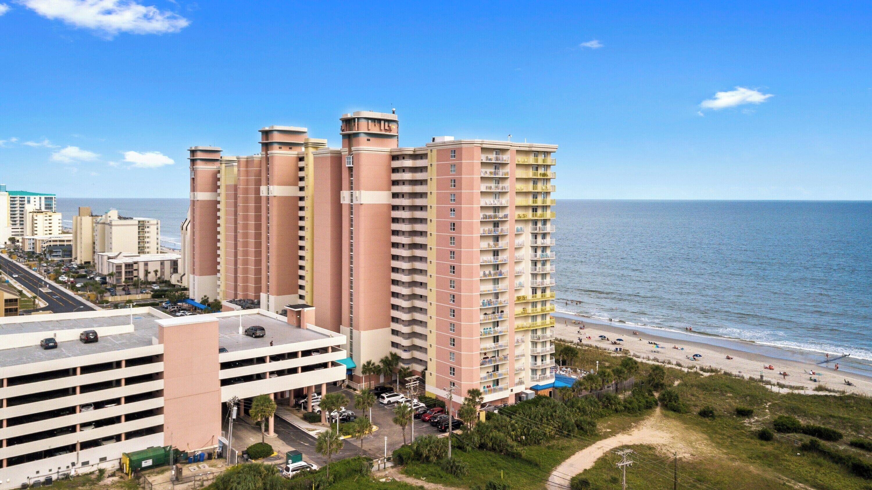 A high-rise hotel with multiple floors, a parking garage, and a beach view.