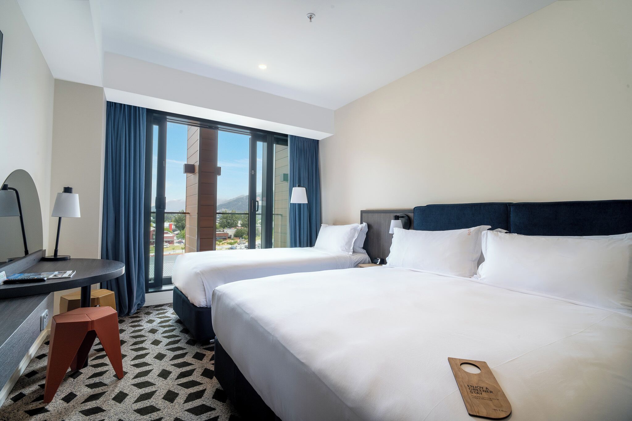 Quarto de hotel com duas camas, uma escrivaninha e vista para o exterior.