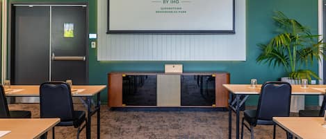 Une salle de conférence dotée d’un grand écran affichant le logo de Holiday Inn, d’un comptoir d’accueil et de plusieurs tables avec des chaises.
