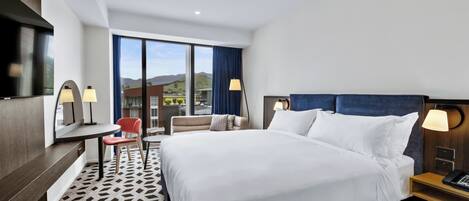 Una habitació d'hotel amb un llit gran, un escriptori amb una cadira, una televisió i una finestra amb vista a les muntanyes.