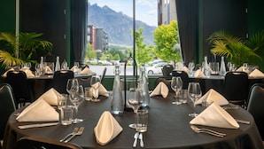 A restaurant table set with glasses, cutlery, and a bottle, with a mountain view through the window. - Holiday Inn Queenstown Remarkables Park by IHG (Queenstown)