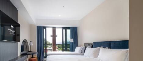 A hotel room with two beds, a flat-screen TV, a desk with a lamp, and a view of the outdoors.