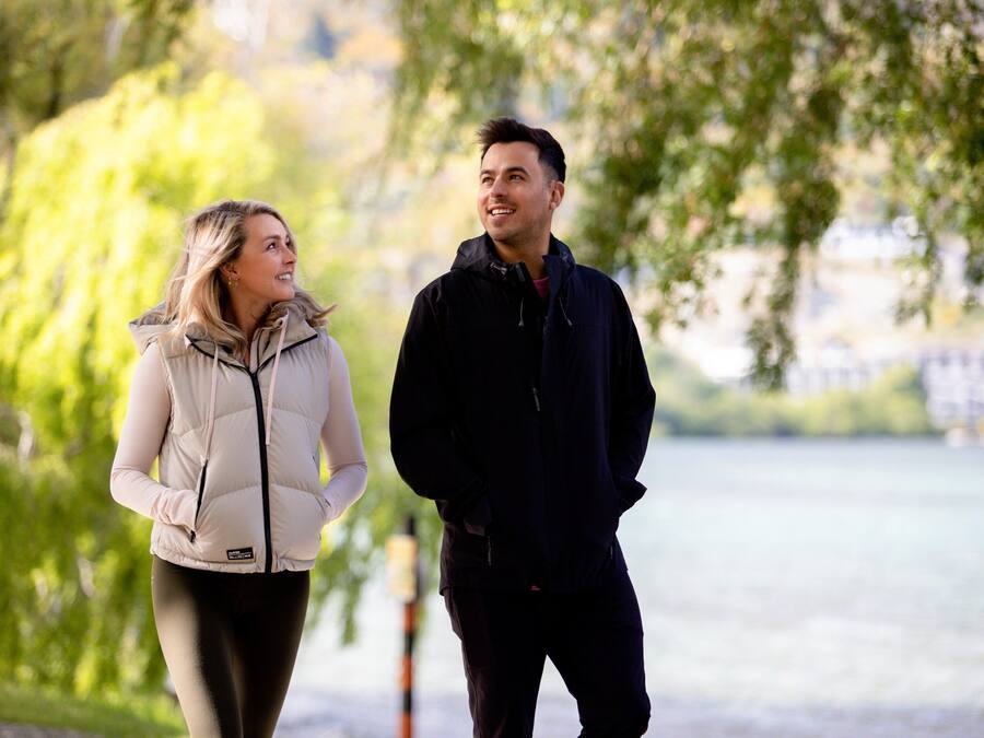 Two people walking by a lake with trees in the background.