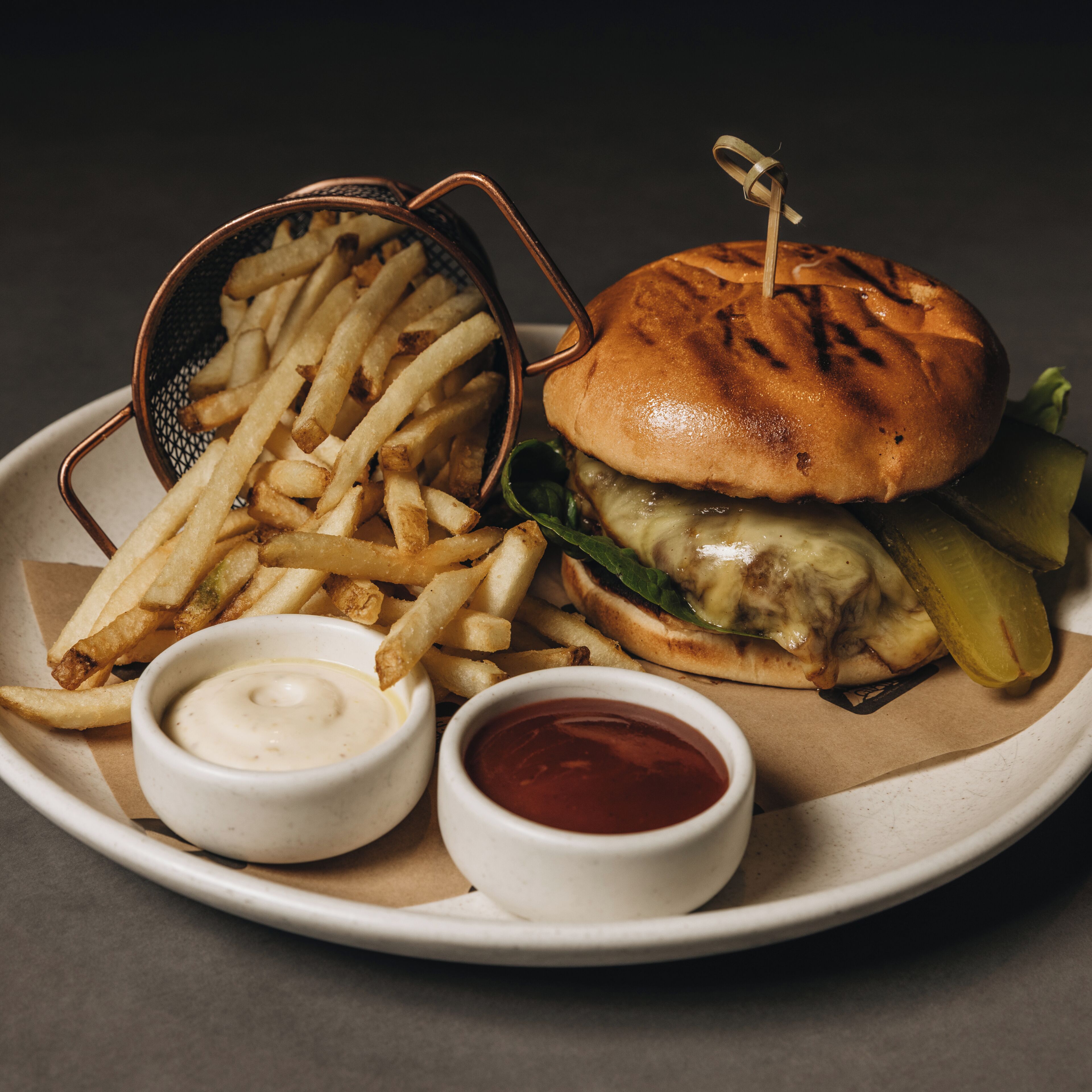 A plate with a burger, fries, and two dipping sauces.