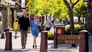 A pedestrian walkway with bollards, a sign for Queenstown Mall, and people walking.