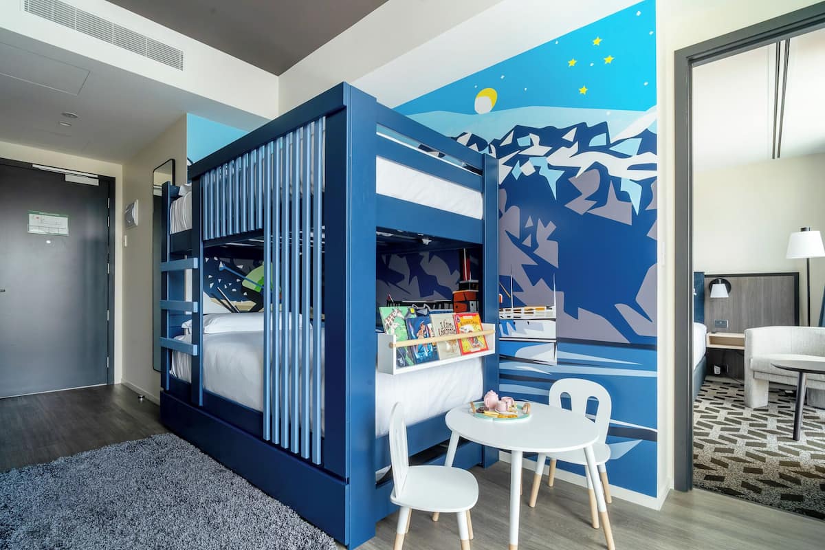 Une chambre avec un lit superposé, une petite table avec des chaises et une fresque murale.