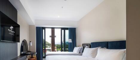 A hotel room with a bed, a desk, a TV, and a view of the outdoors.