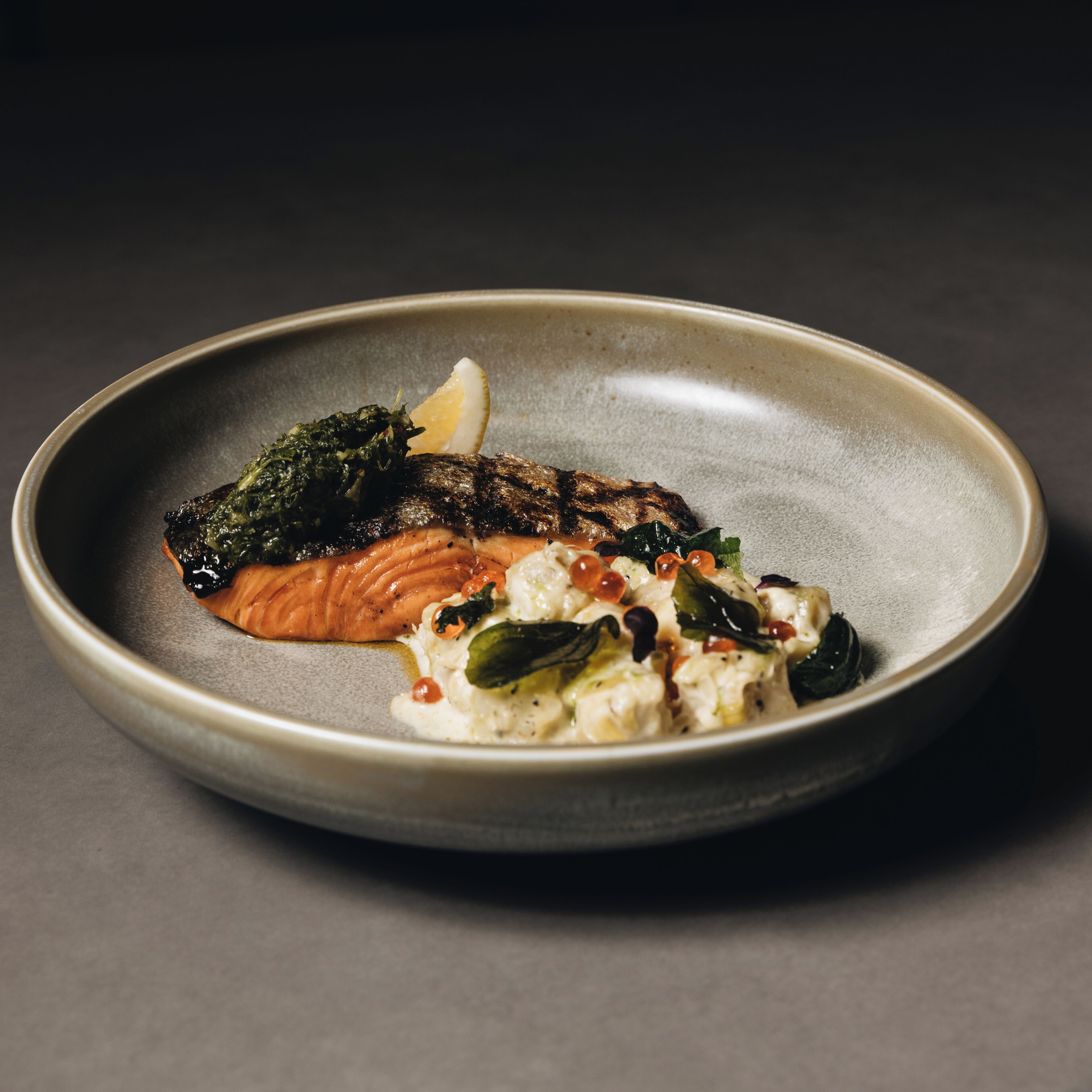 A plate with a piece of grilled salmon, a dollop of sauce, and some greens.
