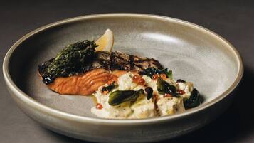 A plate with a piece of grilled salmon, a dollop of sauce, and some greens.