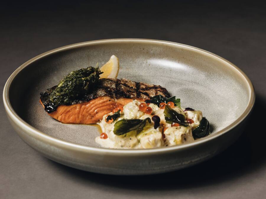 A plate with a piece of grilled salmon, a dollop of sauce, and some greens.