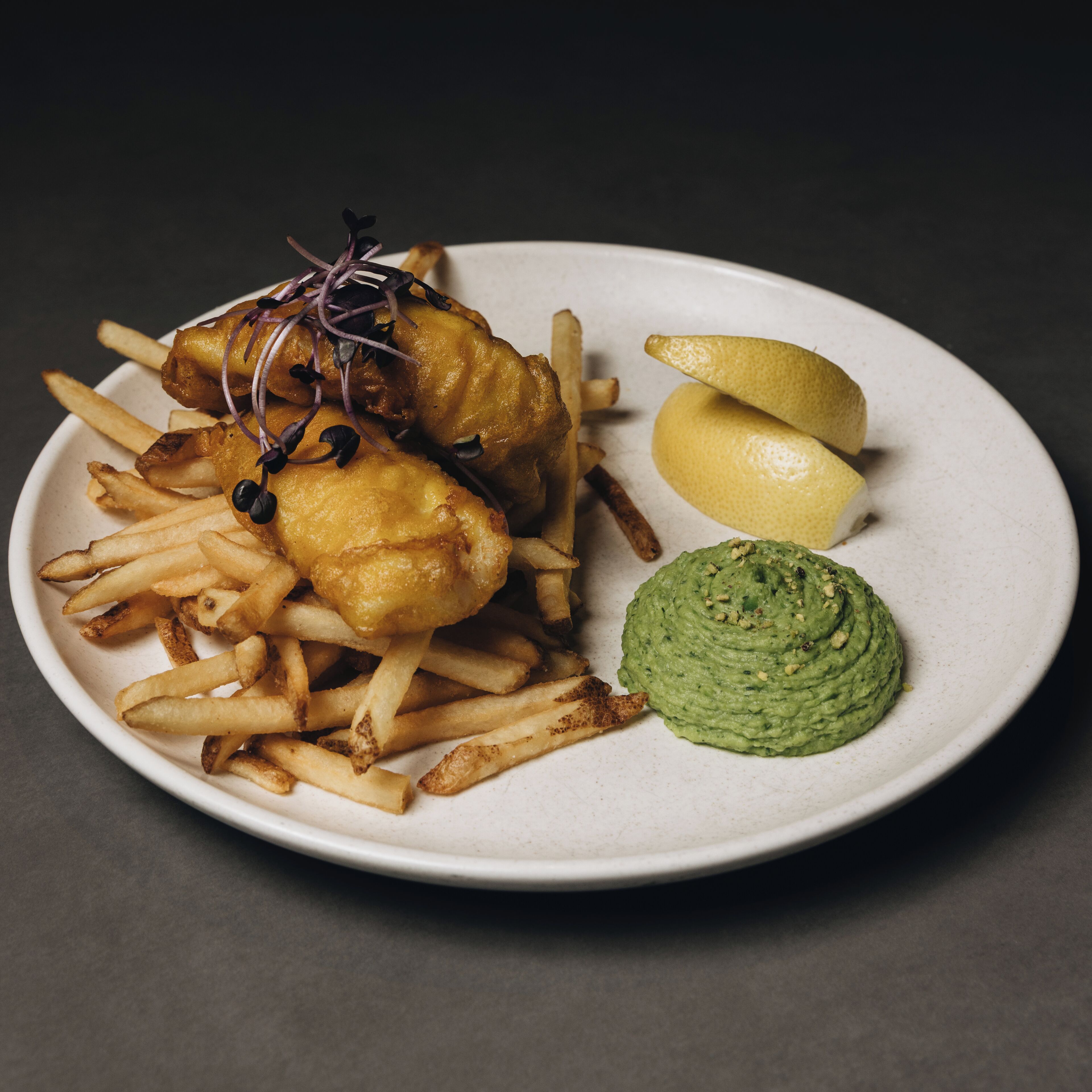 A plate with fish and chips, lemon wedges, and a green sauce.