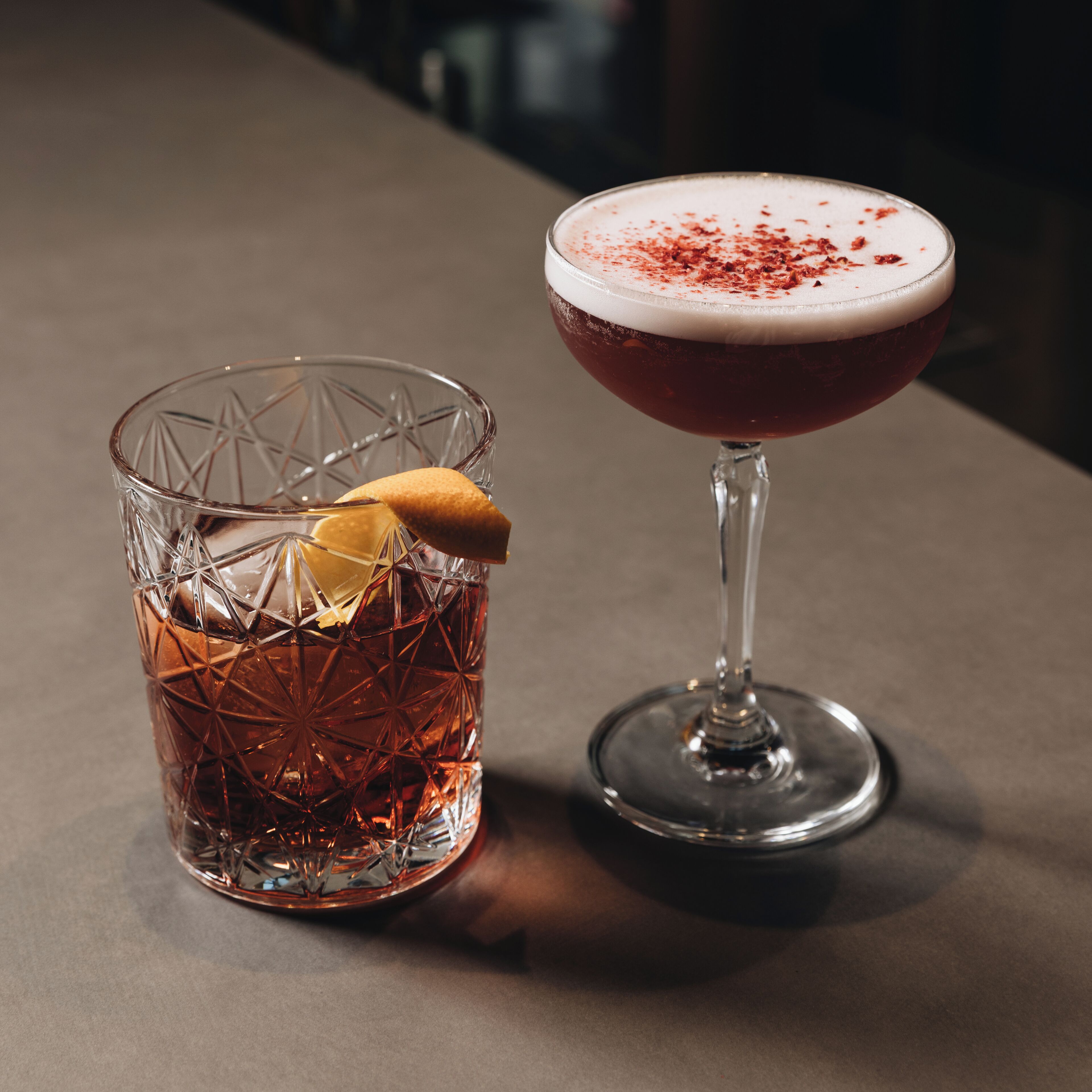 Deux verres contenant des boissons, dont l’un est garni d’une tranche de citron, sont posés sur une table.