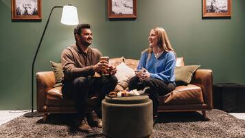 Two people sitting on a leather sofa in a room with green walls, a floor lamp, and framed pictures on the wall.