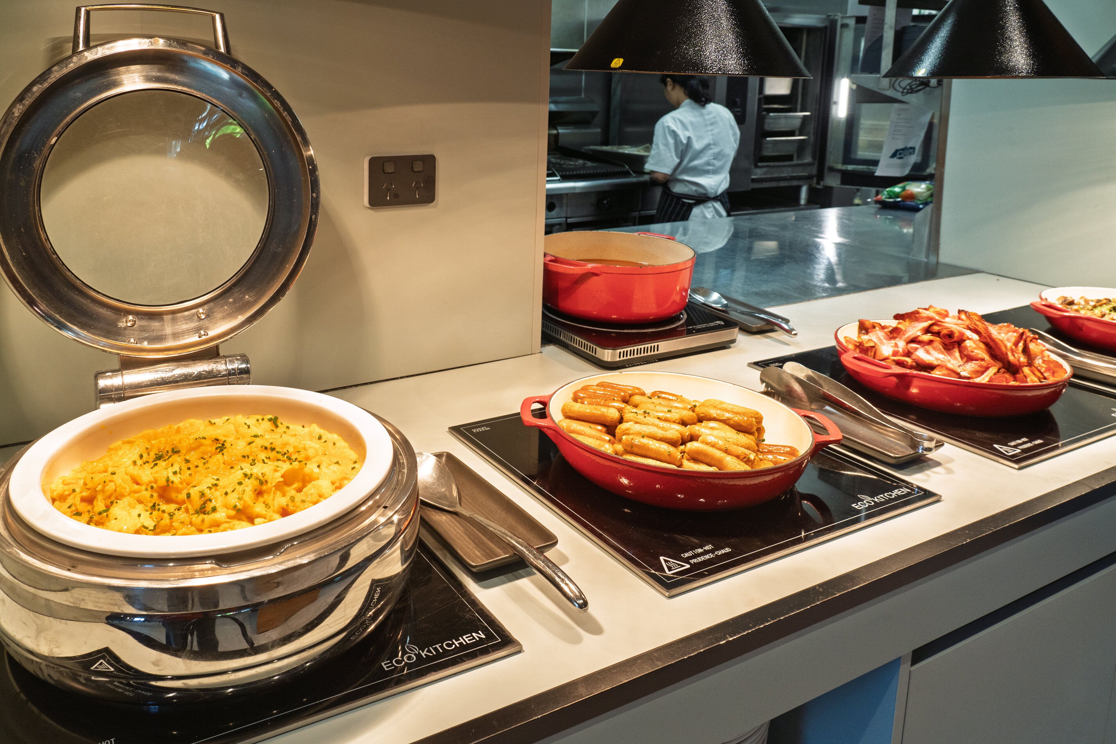 Un buffet proposant divers plats, notamment des pâtes et un plat gratiné, est installé sur un comptoir équipé d’une cuisinière et d’une marmite.