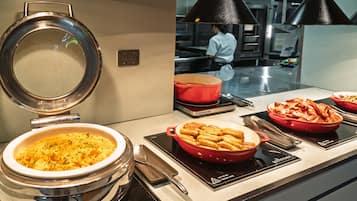 Un buffet proposant divers plats, notamment des pâtes et un plat gratiné, est installé sur un comptoir équipé d’une cuisinière et d’une marmite.