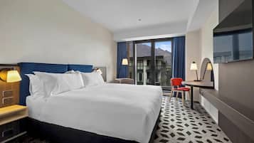 Habitación de hotel con una cama grande, un escritorio, una silla, un televisor y vistas a las montañas a través de la ventana.