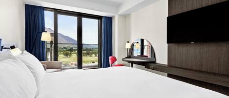 A hotel room with a large bed, a desk with a chair, a flat-screen TV, and a view of the outdoors.