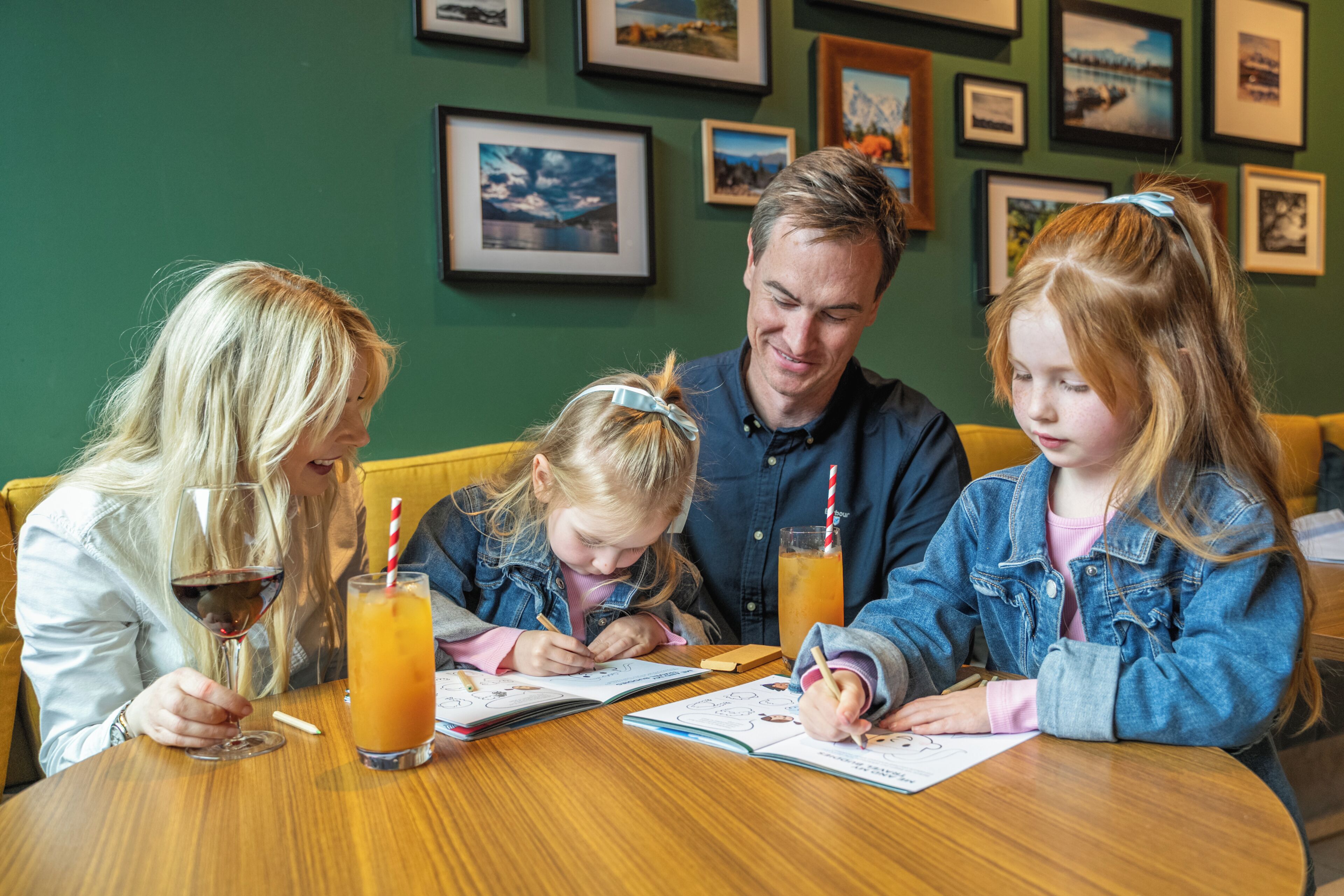 A family dining at a table with a green wall and framed pictures in the background.