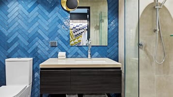 Une salle de bain avec un mur recouvert de carreaux disposés en motif « point de Hongrie », un lavabo moderne avec un miroir, une cabine de douche en verre et des toilettes.