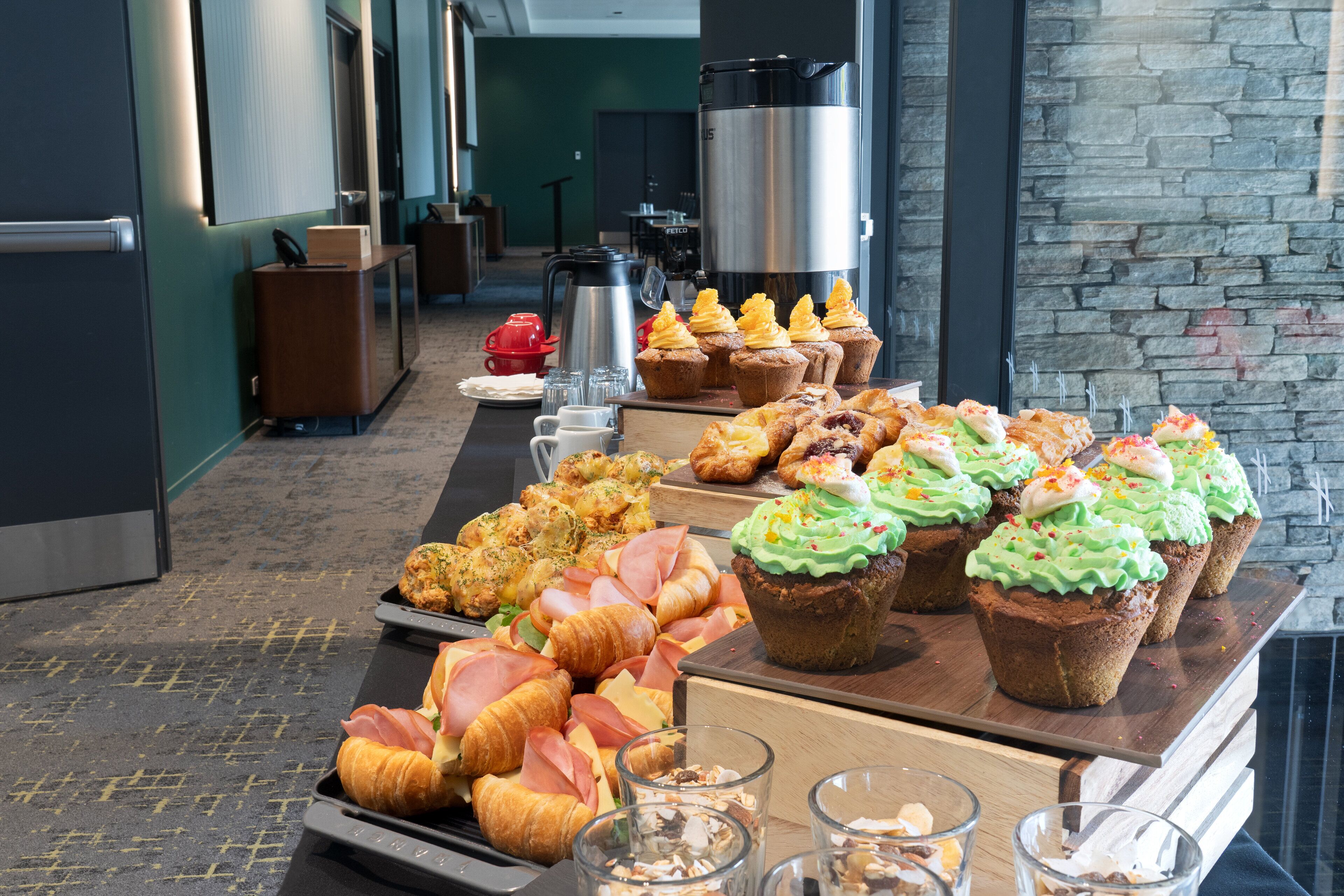 A buffet table with various pastries, including croissants and muffins, and a coffee station with a large coffee pot.