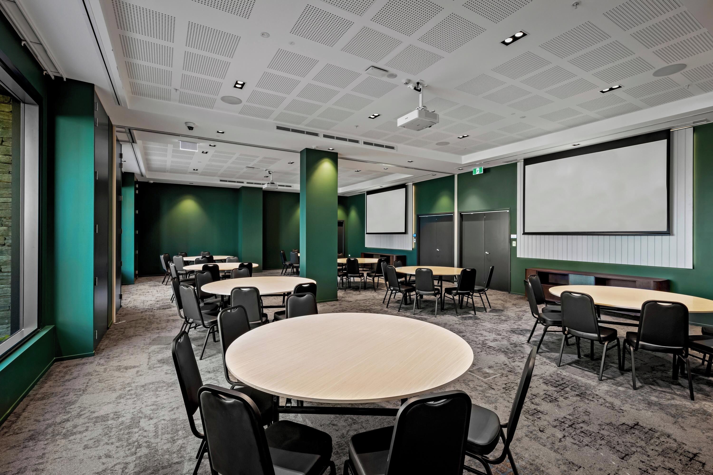 A conference room with round tables, chairs, a projector screen, and a carpeted floor.
