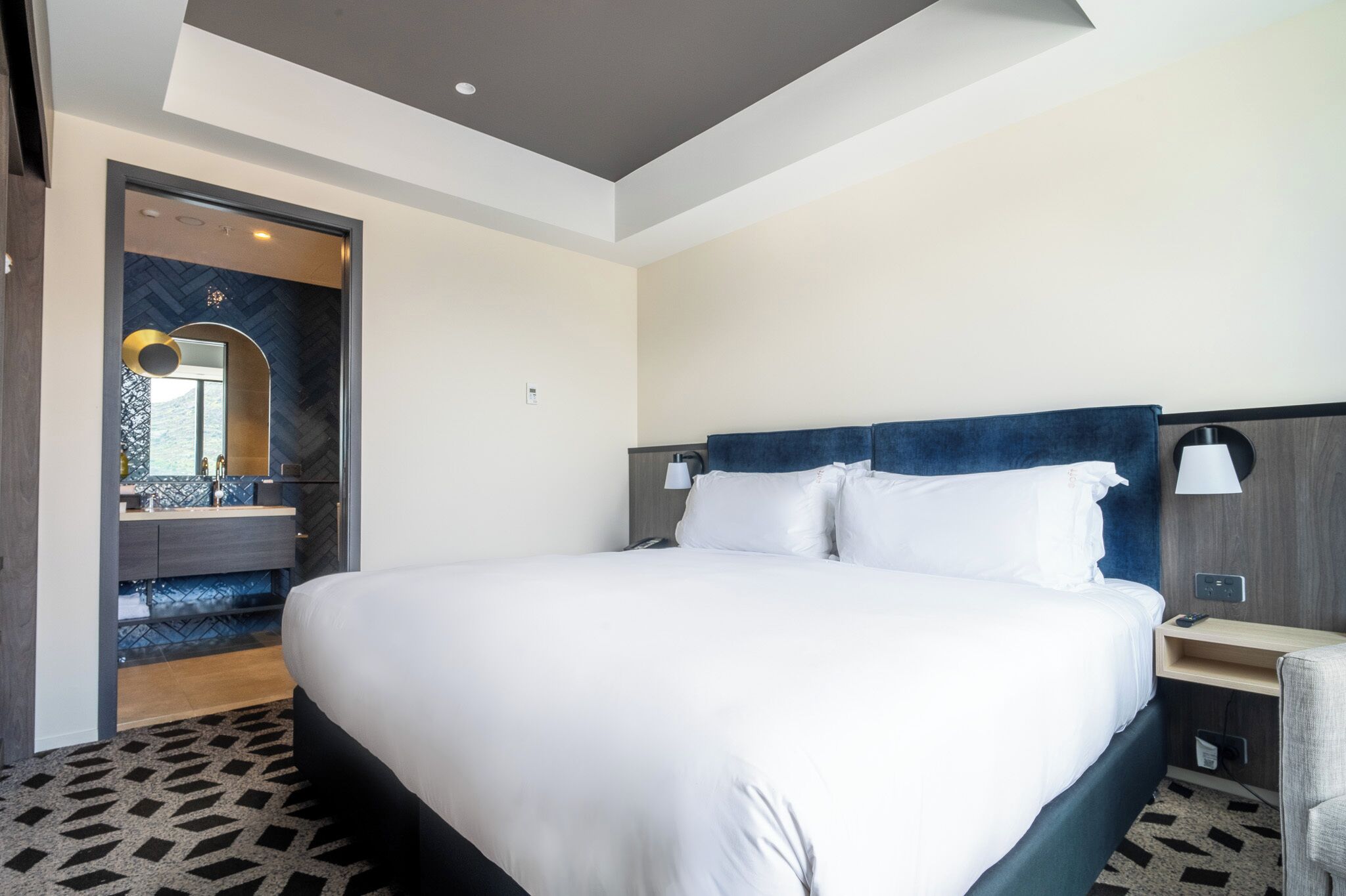 Ein modernes Hotelzimmer mit einem großen Bett, einem Schminktisch mit Spiegel und einer integrierten Sitzbank.