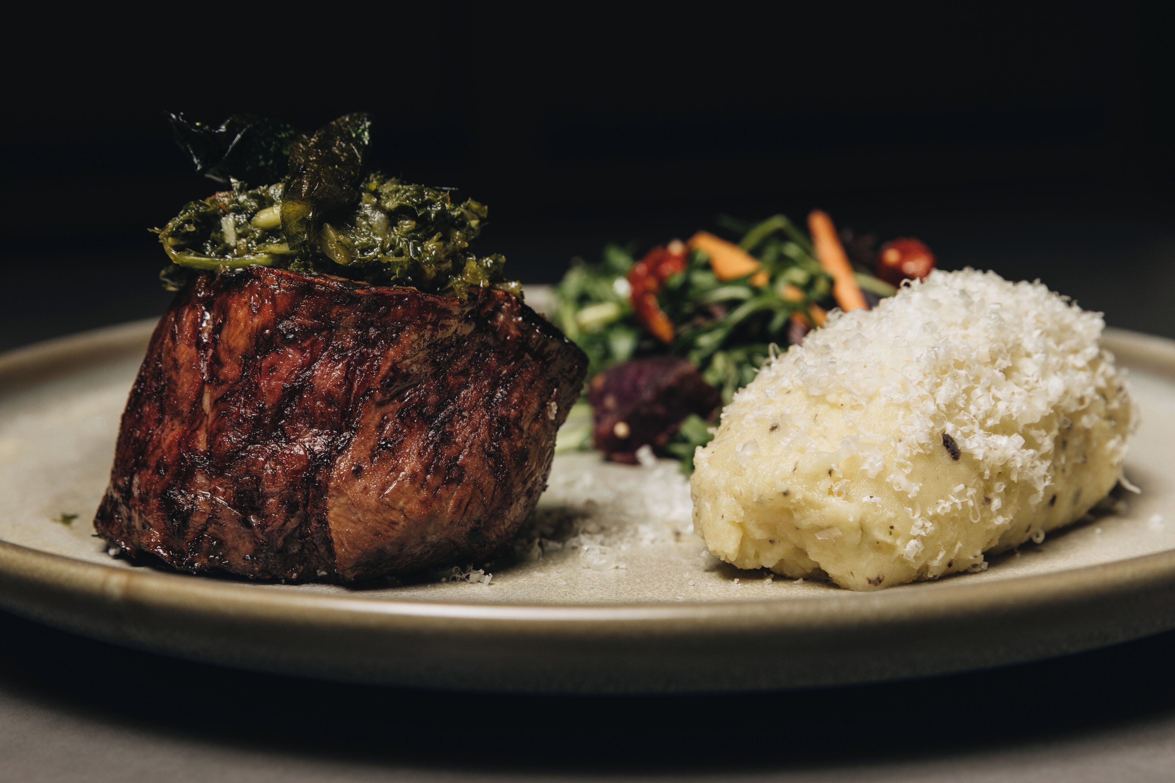 A plate with a grilled steak, a side of mashed potatoes, and a mixed vegetable salad.