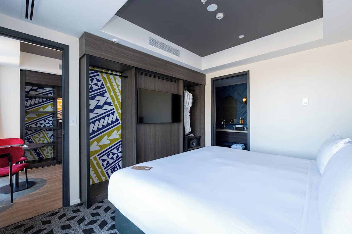 Une chambre d’hôtel avec un grand lit, une télévision, une armoire et un fauteuil rouge.