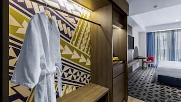 Ein Hotelzimmer mit einem Bett, einem Schreibtisch, einem Stuhl, einem Fernseher und einem Bademantel, der an einem Gestell hängt.