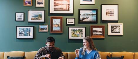 Un comedor con una mesa de madera, dos personas sentadas y una pared decorada con fotografías enmarcadas de paisajes.