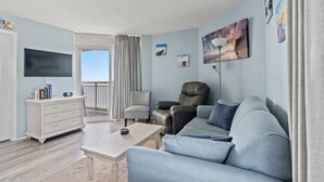 A modern living room with a sofa, armchair, and a flat-screen TV mounted on the wall. - Bay Watch 1241-1BR/1BA Oceanfront Condo in North Myrtle Beach (North Myrtle Beach)