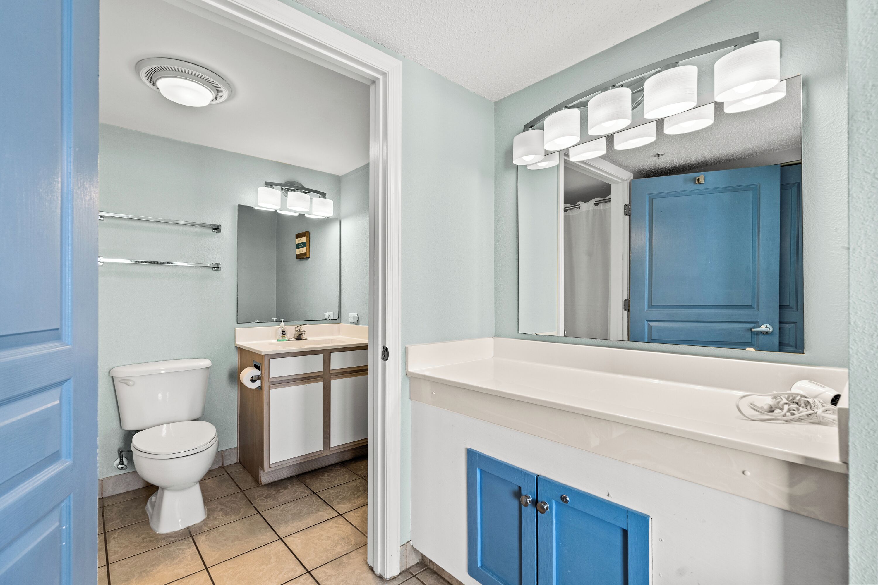 Une salle de bain avec des toilettes, un lavabo, un miroir et un meuble bleu.